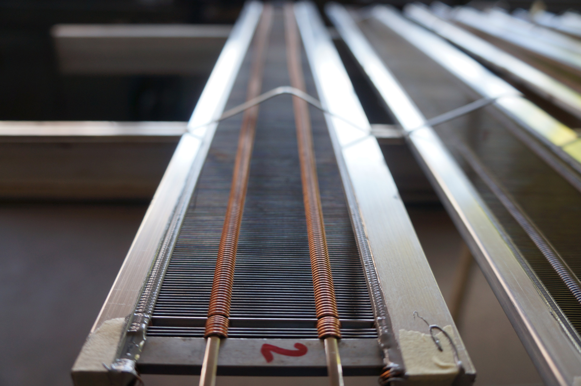 Feine Metallstäbe und kupferfarbene Bindungen eines Webblatts in der Niesing-Werkstatt